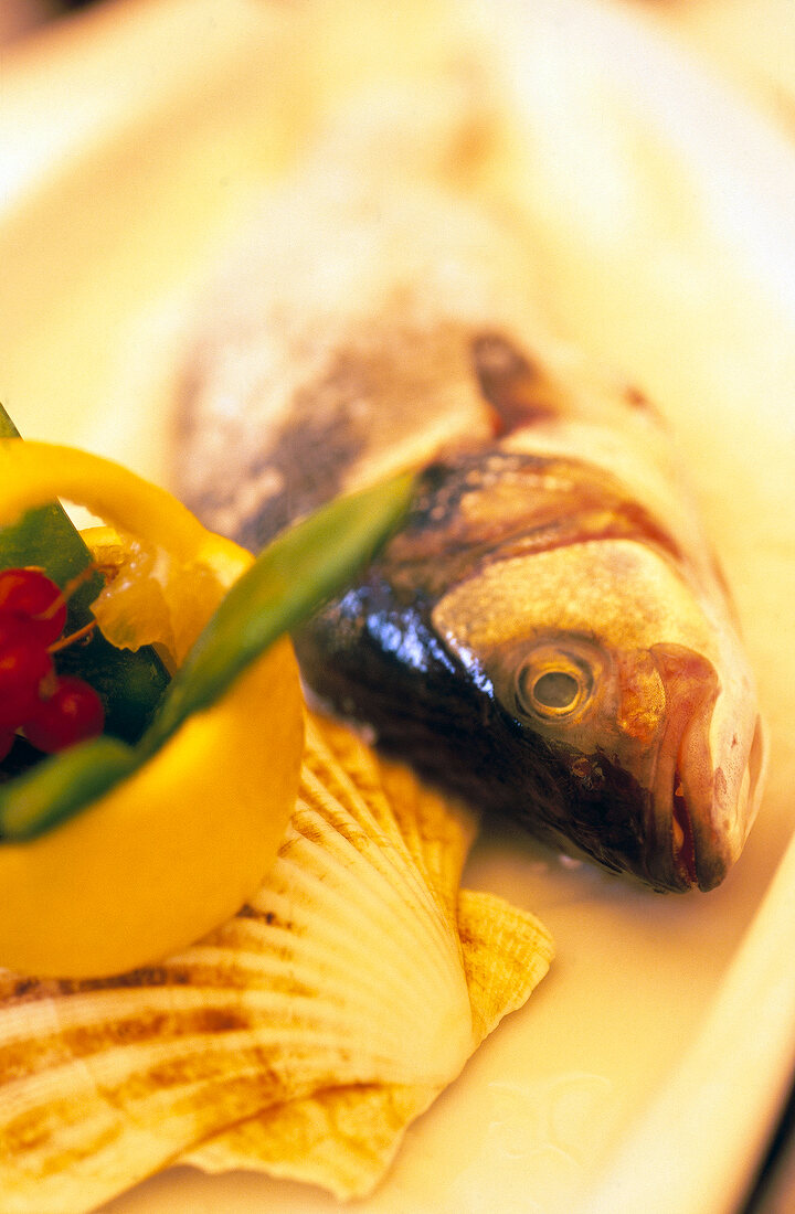 ganzer Fisch mit Paprika und Muschel auf weißem Teller