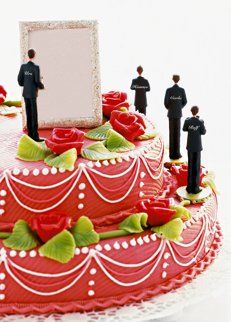 Close-up of wedding cake decorated with roses, bride figurines and picture frames