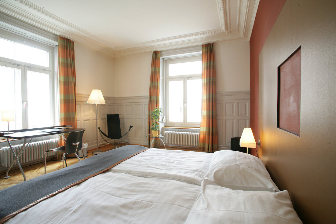 Interior of bedroom with bed, cushion, table, lamp and curtains in hotel, Switzerland