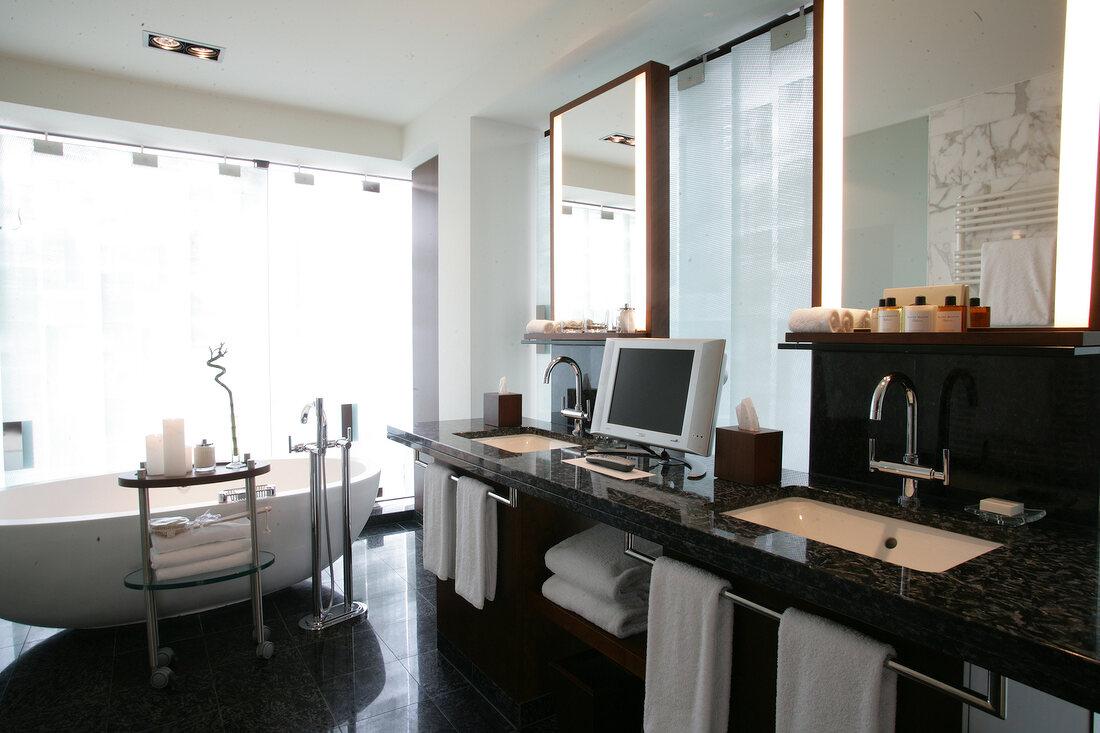 Bathroom with bathtub, TV, washbasin and towels in hotel, Switzerland