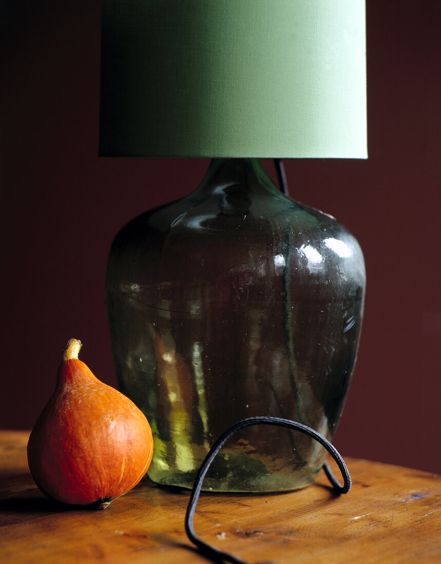 Close-up of lamp with green glass and small pumpkin on table