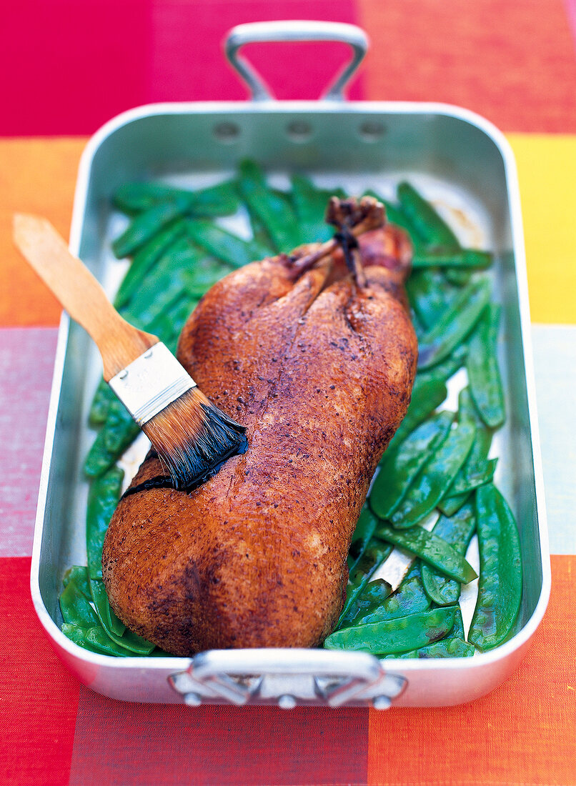 Roasted duck with vinegar and caramel sauce in roasting dish with basting brush