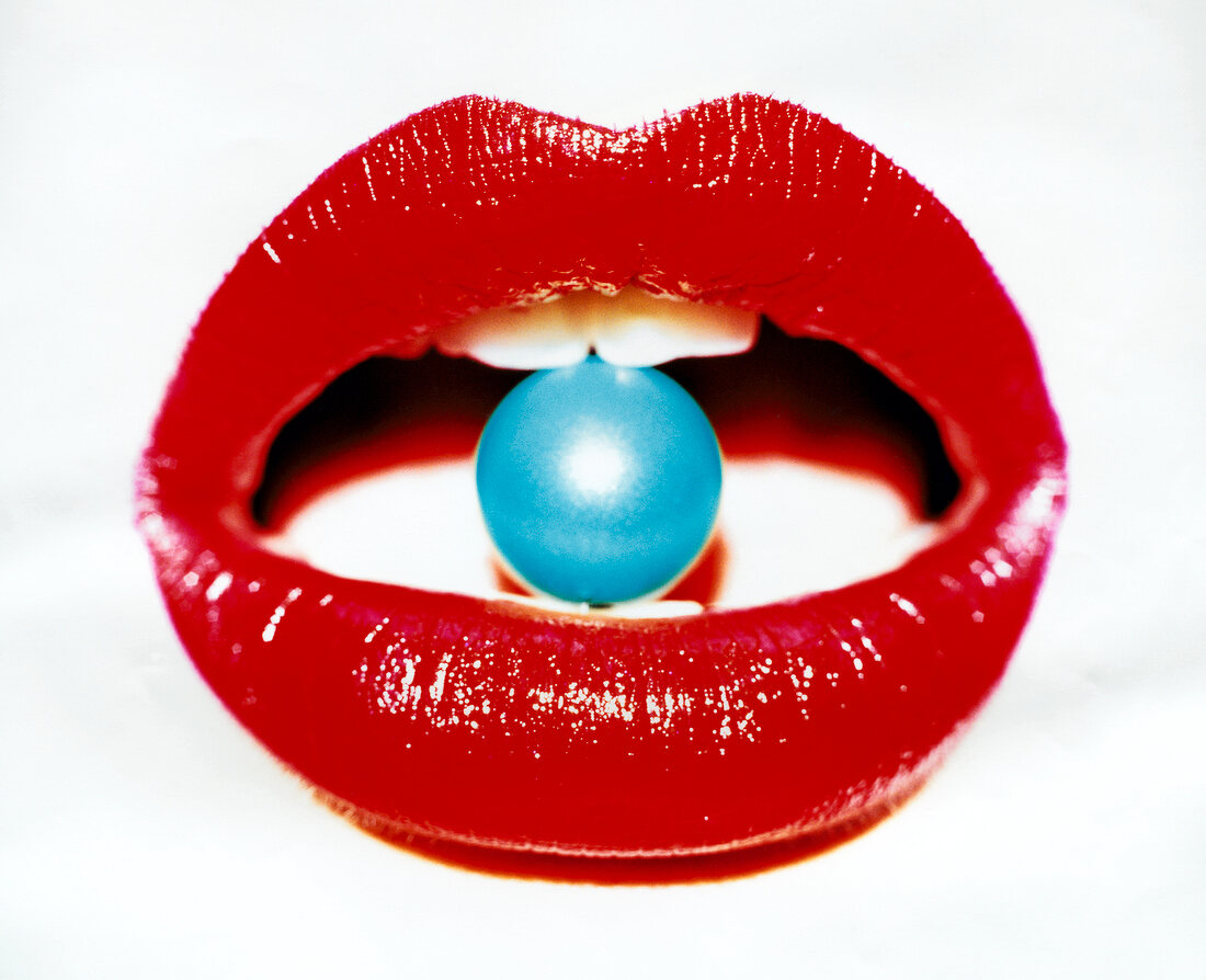 Close-Up of woman's lips with red lipstick holding blue hydro-pearl between teeth