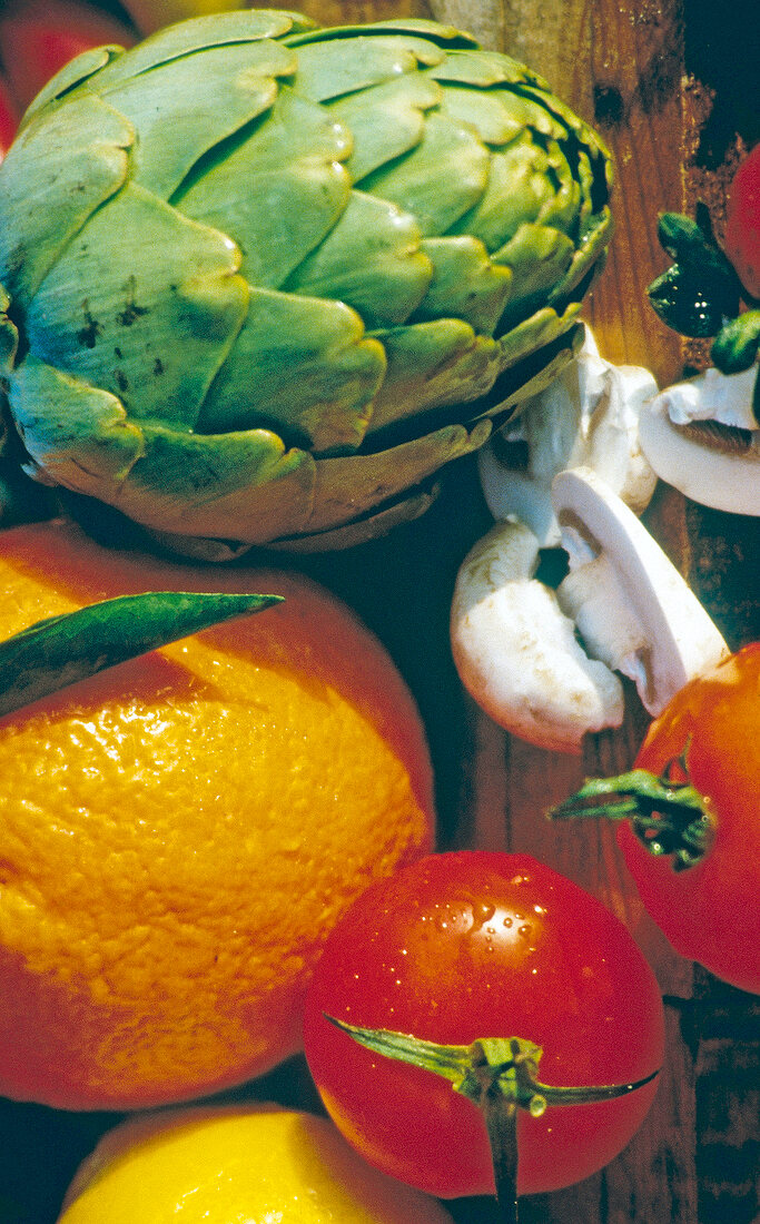 Close-up of various foods like orange, artichoke, mushrooms and tomato