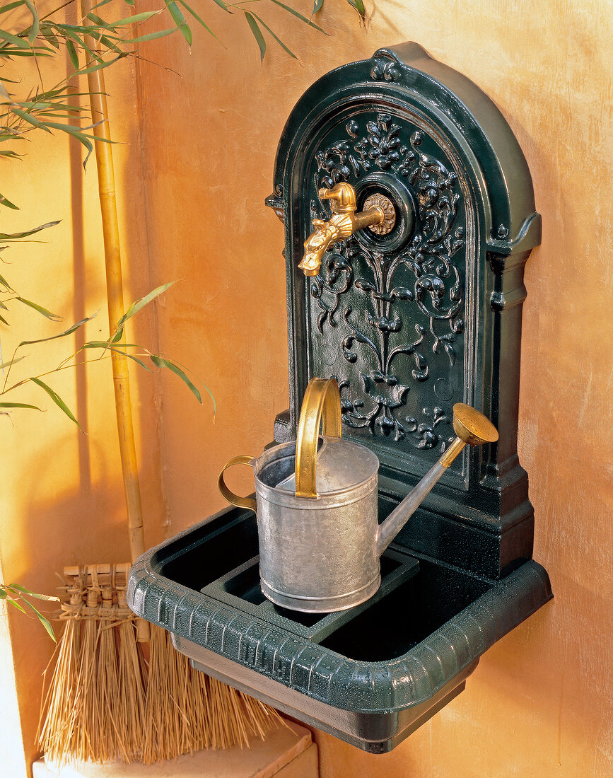 Watering can on wall fountain made of cast iron
