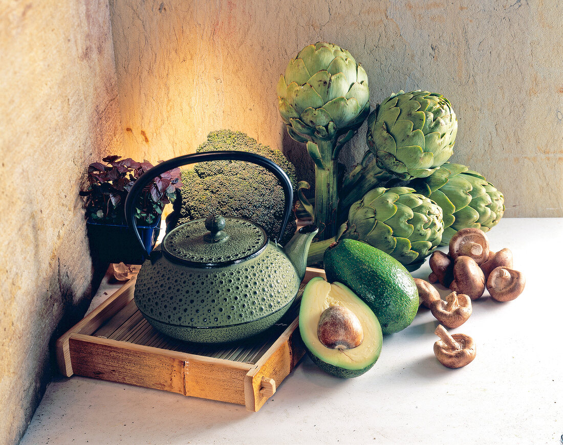 Healthy diet comprising of artichokes, avocados and mushrooms with teapot on wooden tray