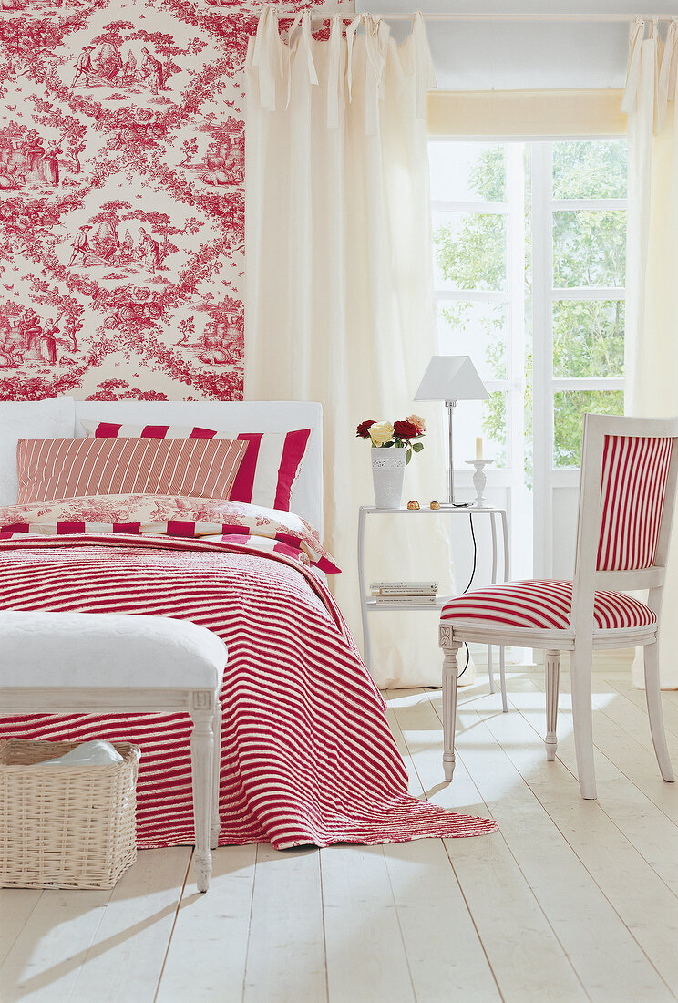 Chair and bed with red striped bed sheet and cushion in bedroom
