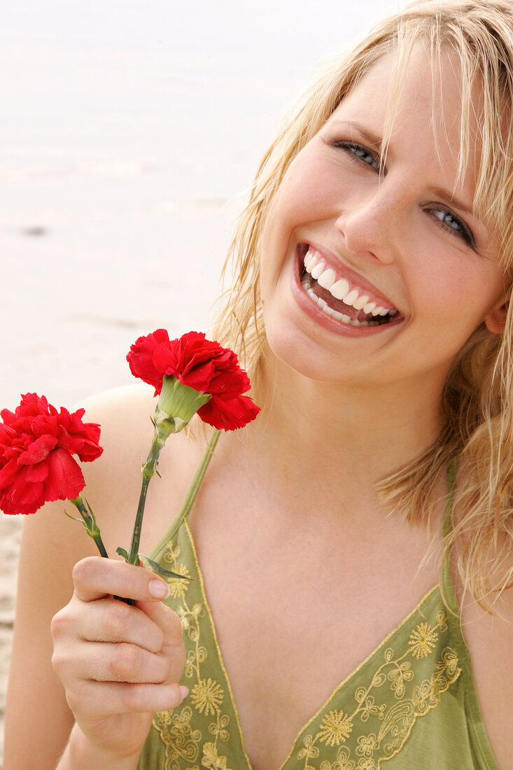 Woman wearing green halterneck dress holding red flower on beach, laughing