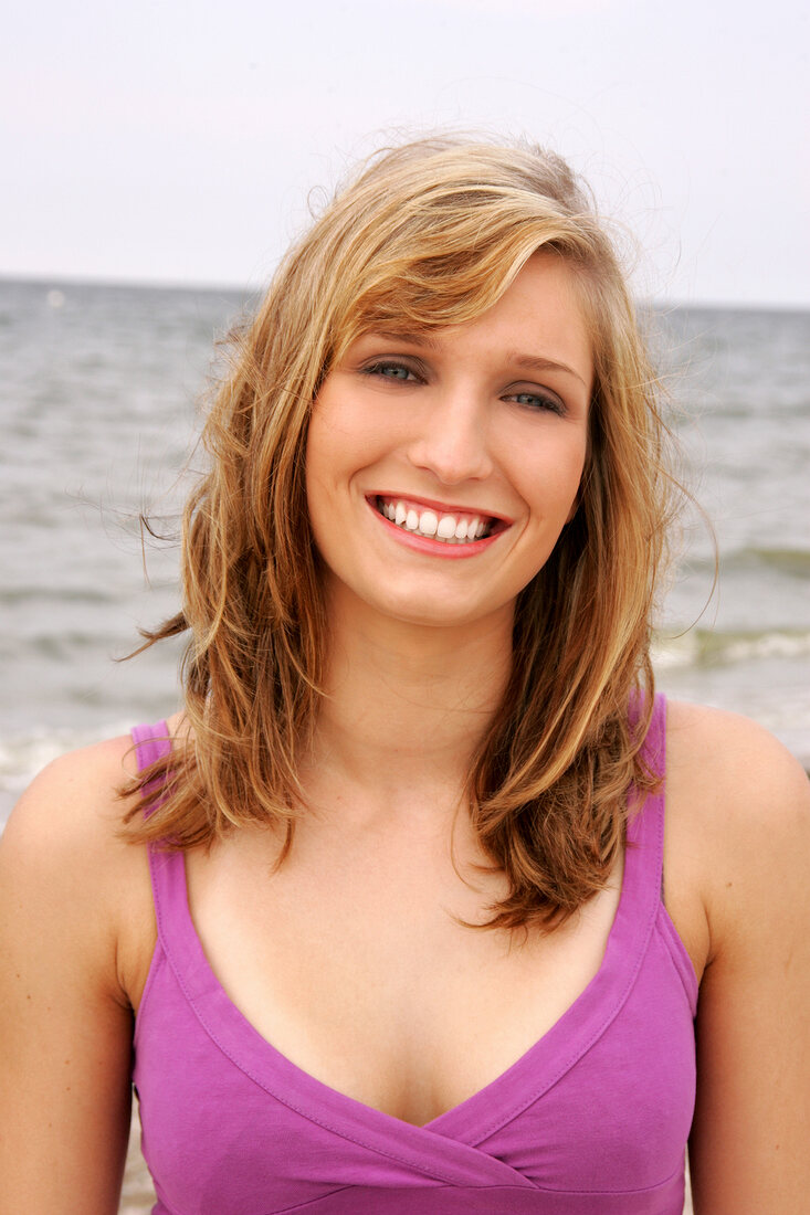 Portrait of beautiful woman wearing purple top standing on beach, smiling