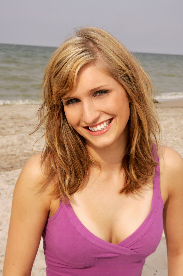 Portrait of beautiful blonde woman wearing pink top standing on beach, smiling