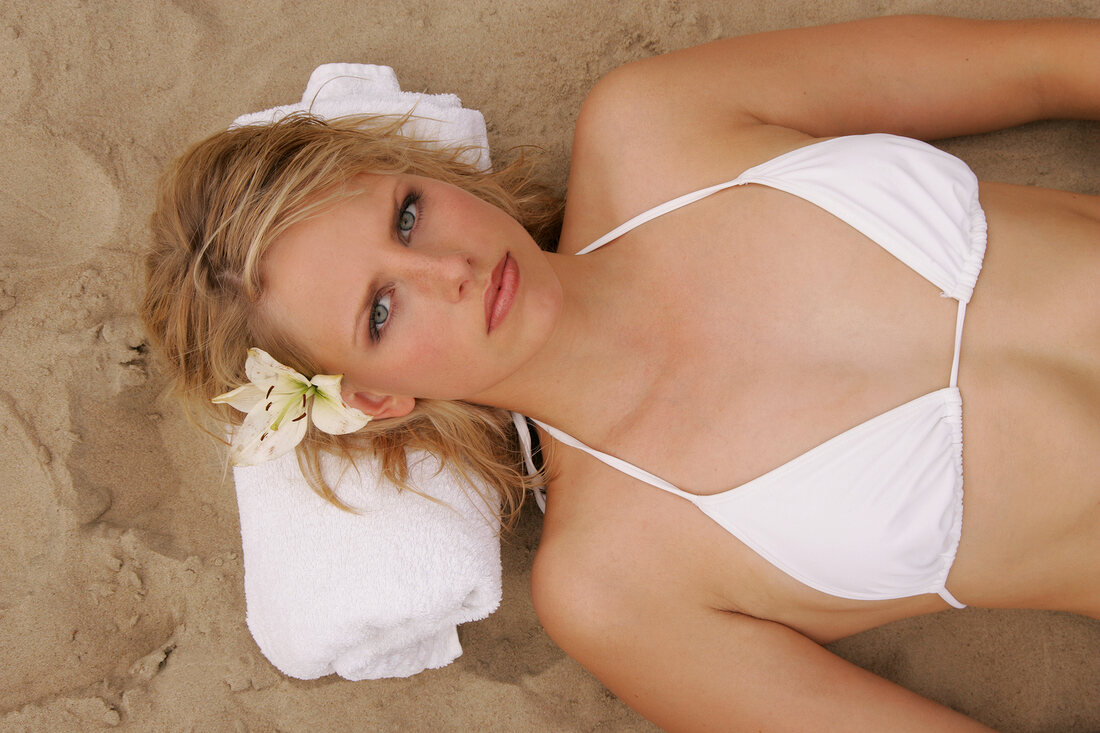 Overhead view of angry woman wearing white bikini lying on sand with towel under head