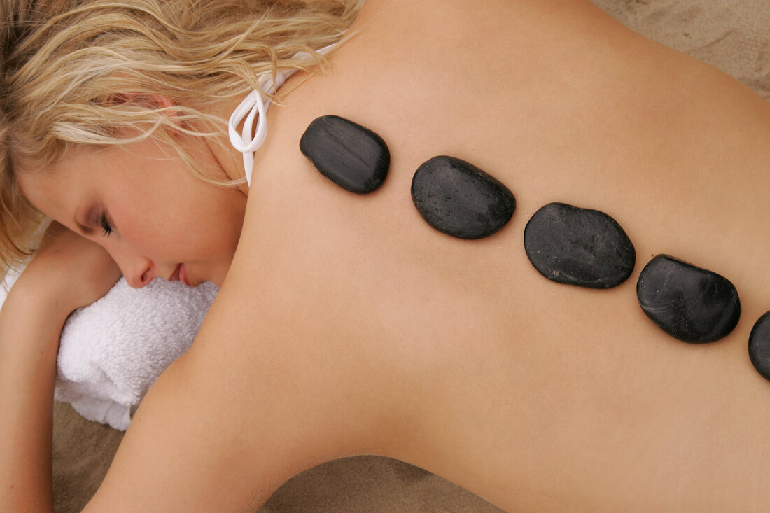 Rear view of blonde woman lying on beach with stones on her back