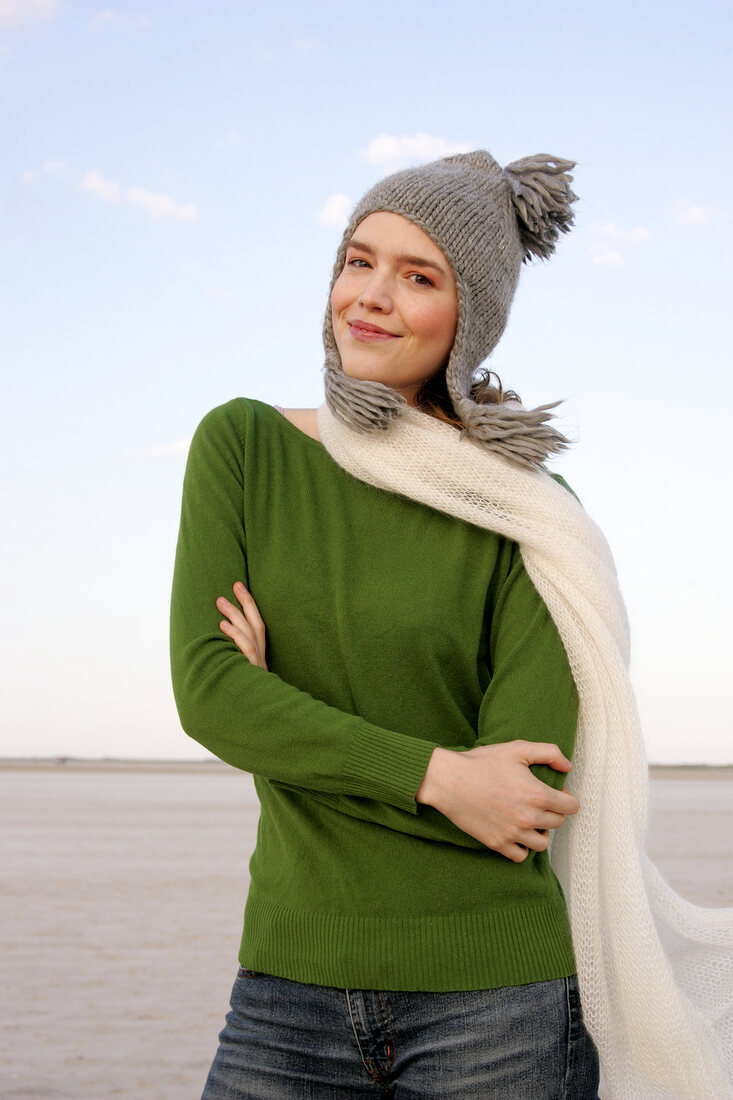 Beautiful woman wearing green sweater, jeans and scarf standing with arms crossed, smiling