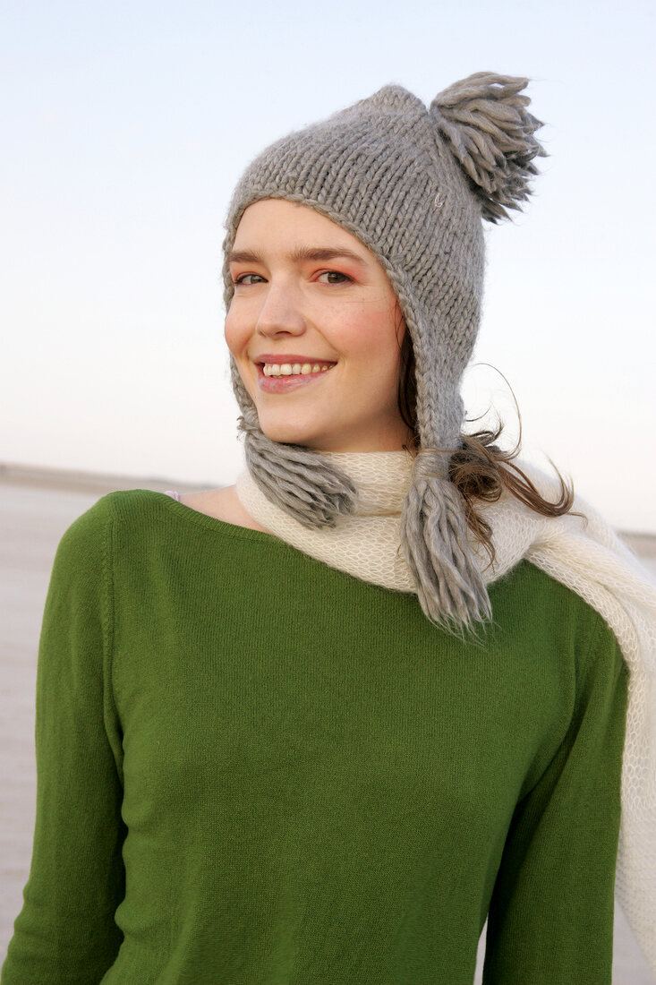 Beautiful woman wearing green sweater, jeans and scarf standing with arms crossed, smiling