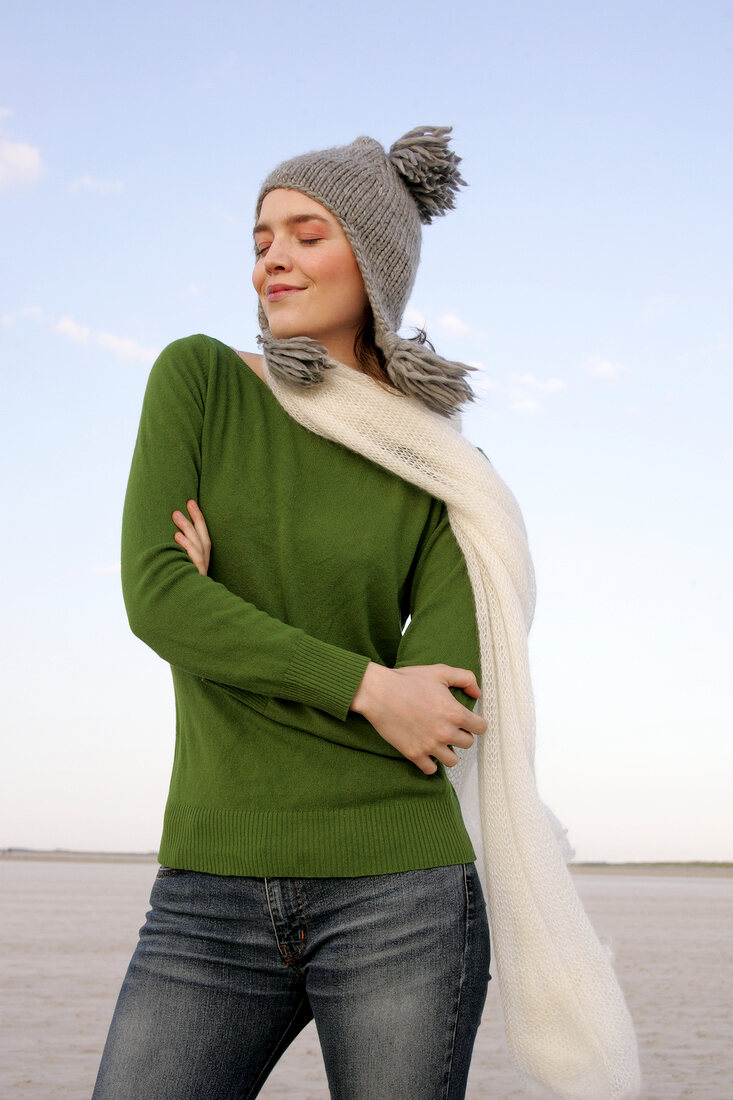 Beautiful woman wearing green sweater, jeans and scarf standing with arms crossed, smiling