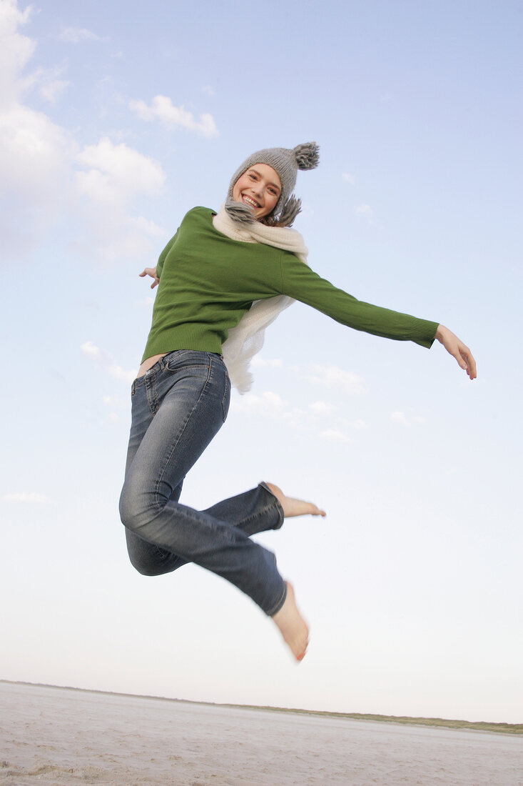 Beautiful woman wearing green sweater, jeans and cap jumping in air, smiling widely