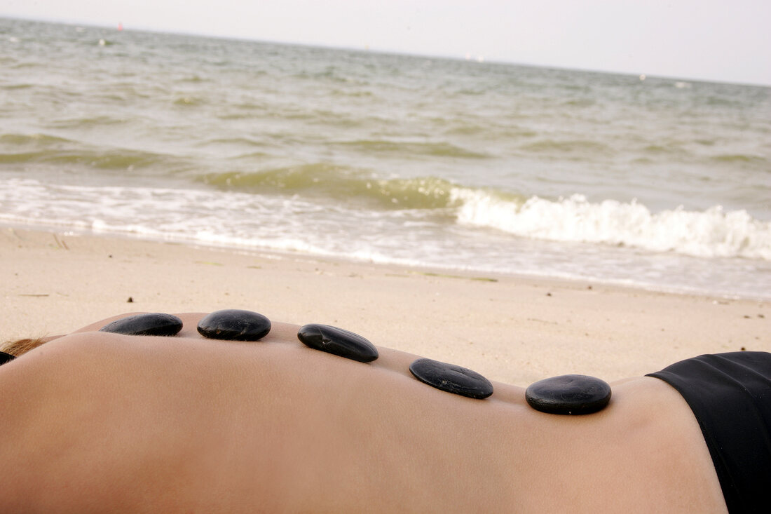 Rear view of blonde woman lying on beach with stones on her back