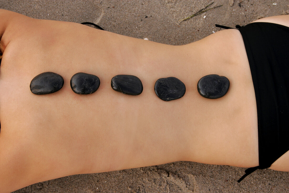 Semi-nude woman lying on sand with massage stones placed on back, mid section