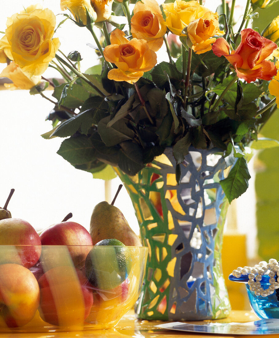 Close-up of fresh flowers in vase and glass bowl of fruits on table