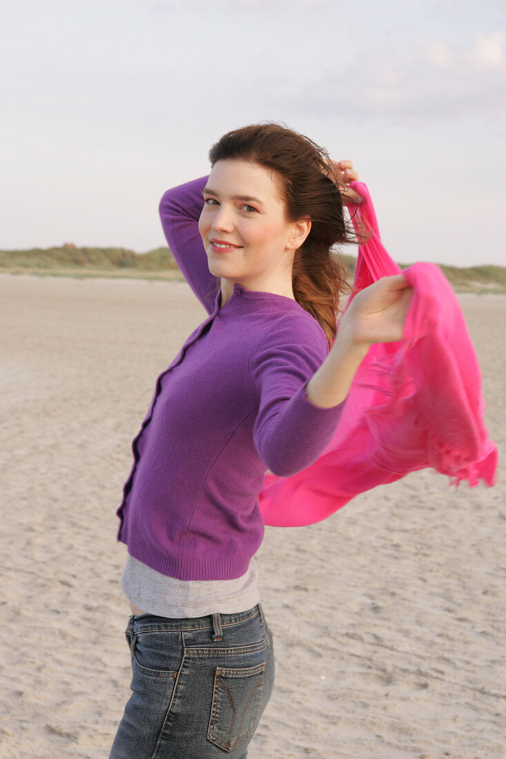 Portrait of pretty woman wearing purple sweater and pink shawl standing on beach, smiling