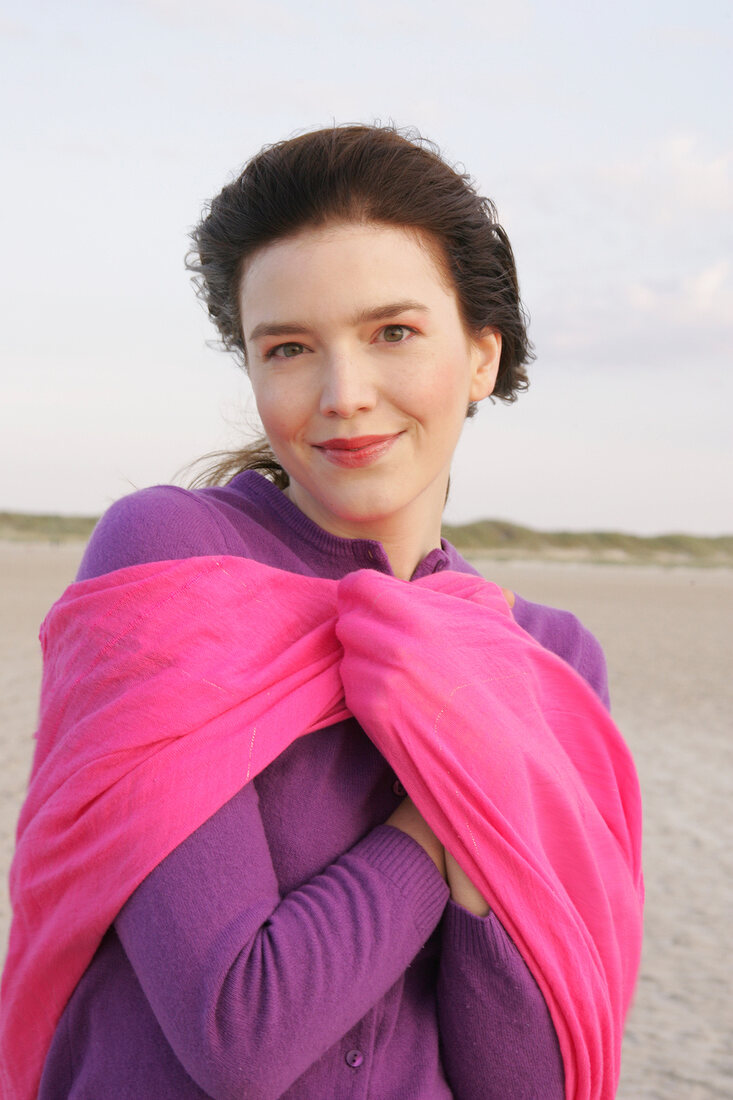Portrait of pretty woman wearing purple sweater and pink shawl standing on beach, smiling