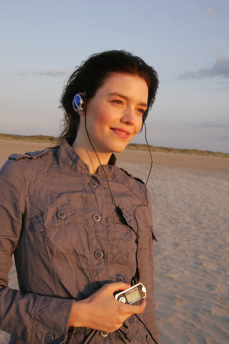 Pretty woman wearing brown shirt and jeans listening music, looking away and smiling