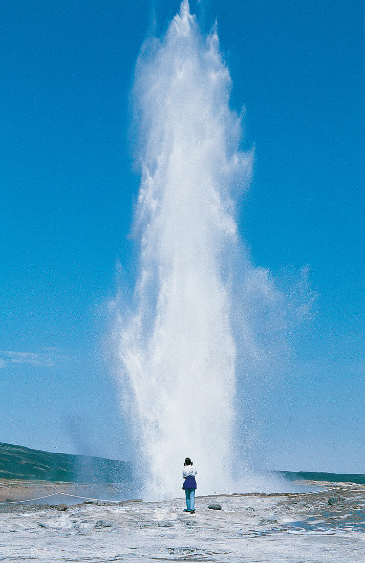 Wasserfontäne davor ein Mensch, blauer Himmel.