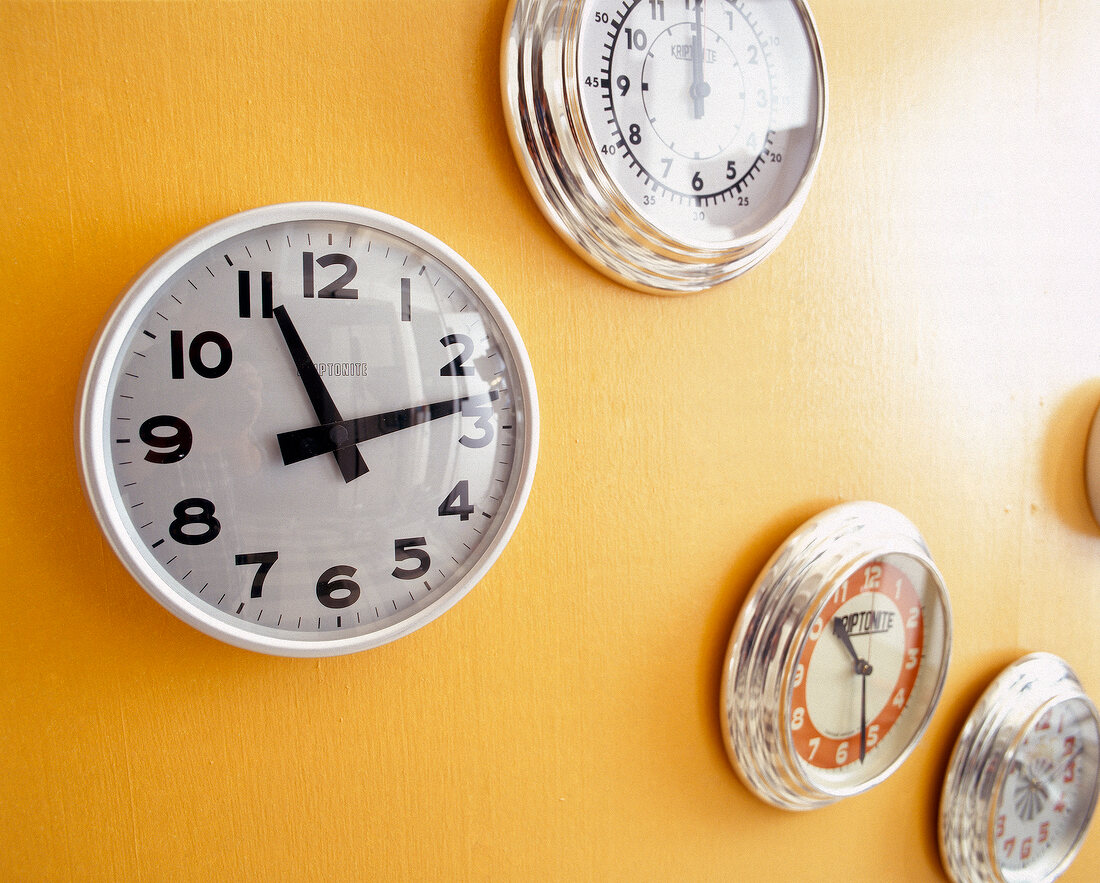 weiße runde Wanduhr mit großen Ziffern an gelber Wand + and. Uhren