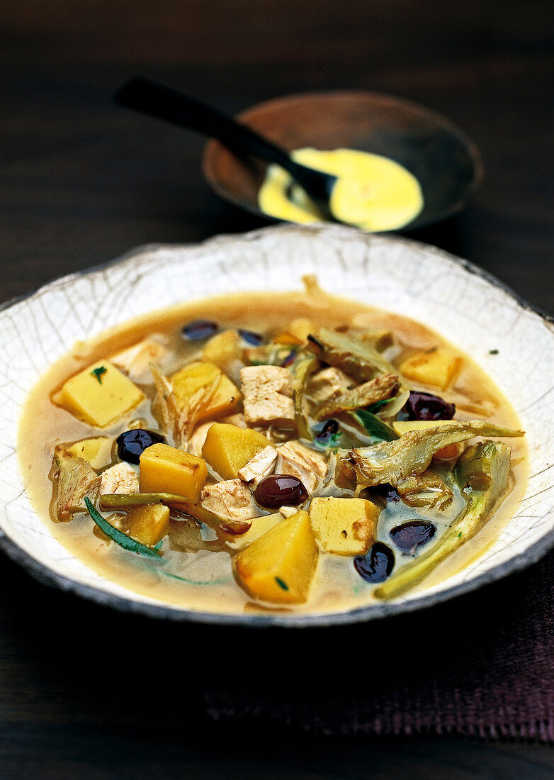 Chicken soup with olives and potatoes served in rustic dish