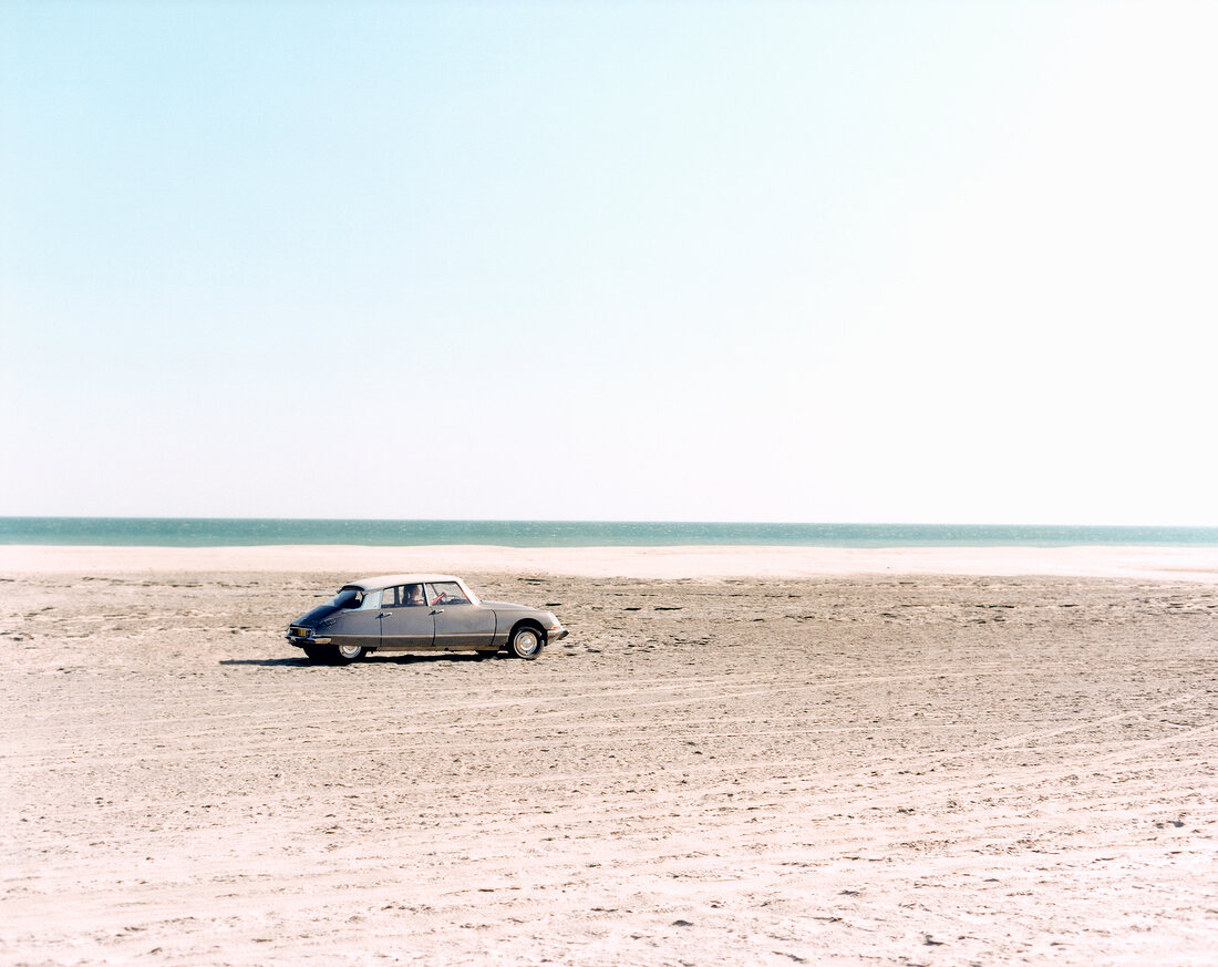 Auto mit Fahrerin am Strand vor dem Meer