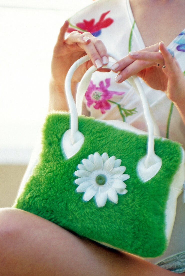 Close-up of woman holding green plush handbag with white blossom