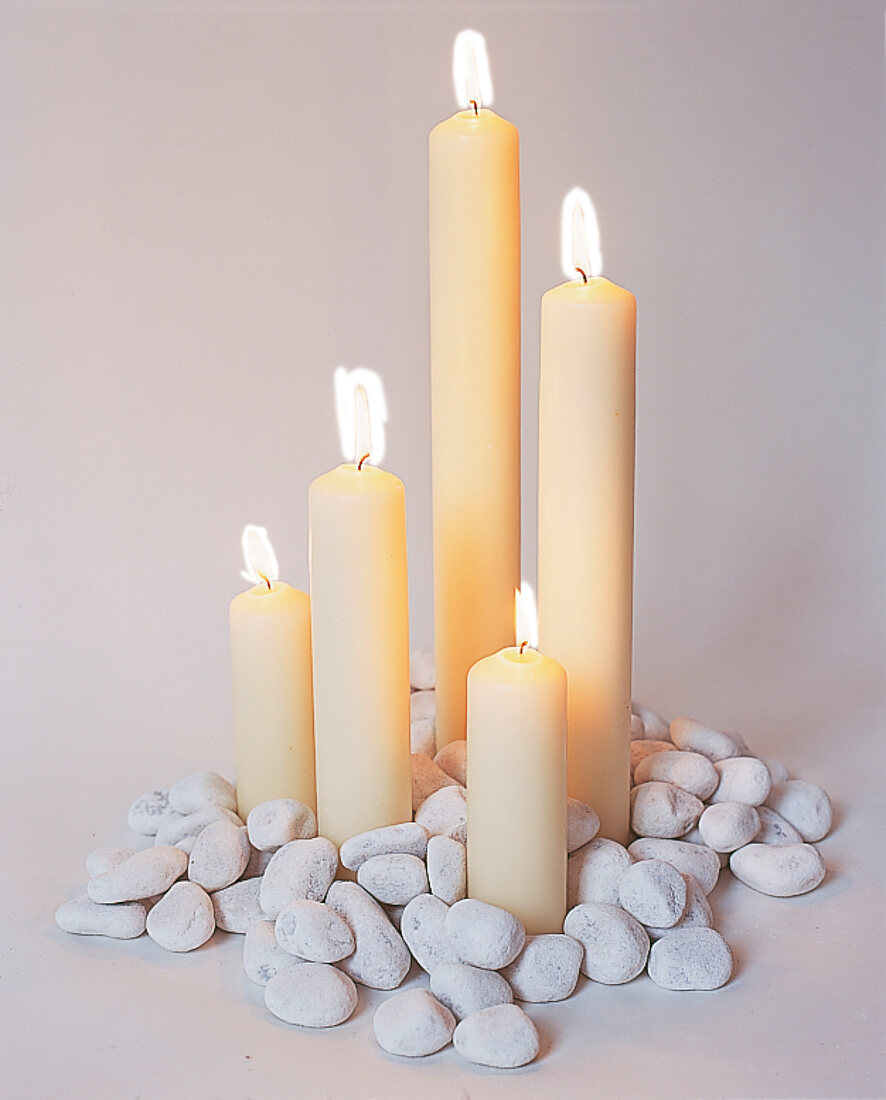 5 weiße brennedne Kerzen stehen auf Haufen Kieselsteine, Dekoration