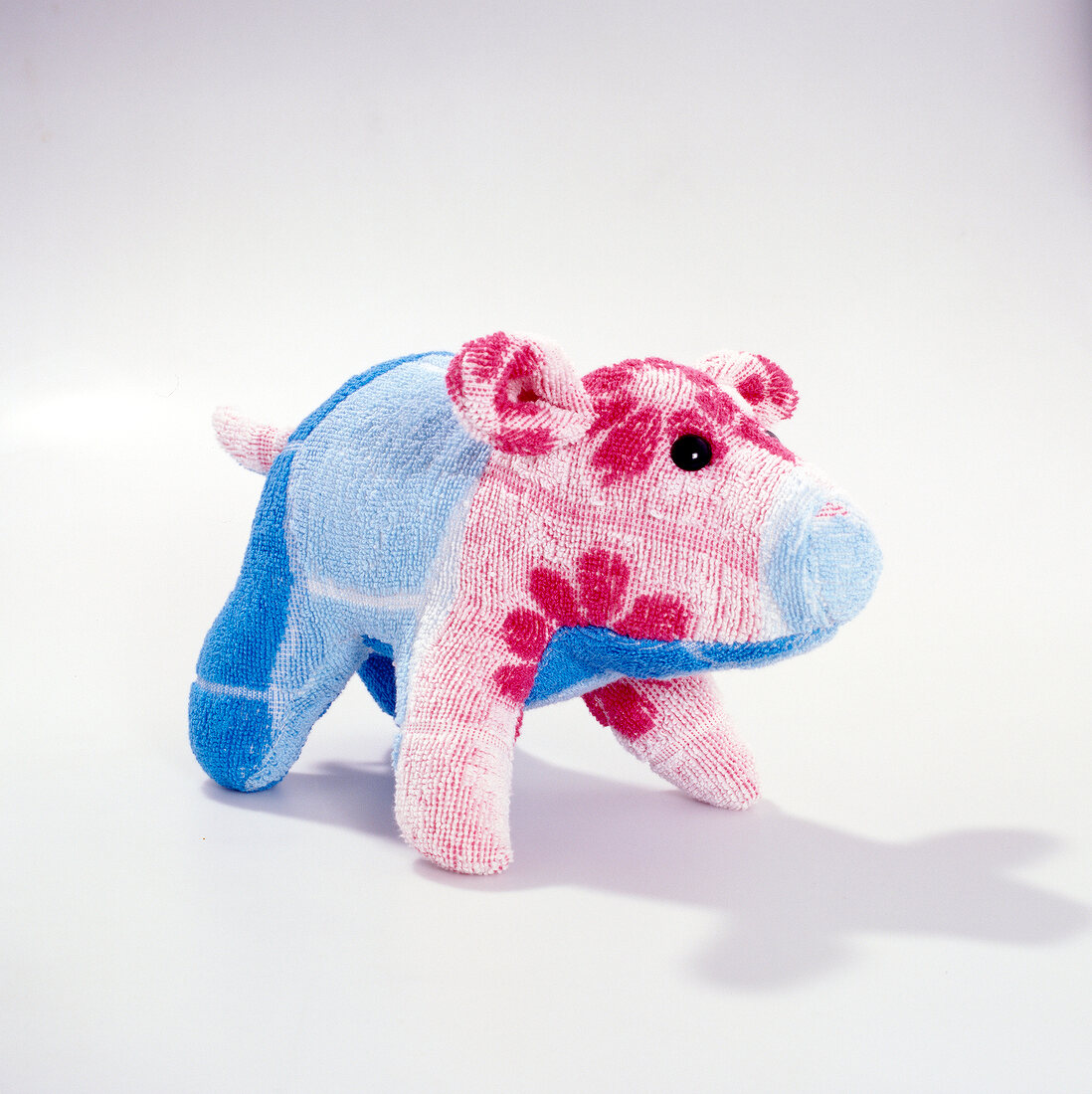 Close-up of pink and blue pig shaped stuffed figurine on white background