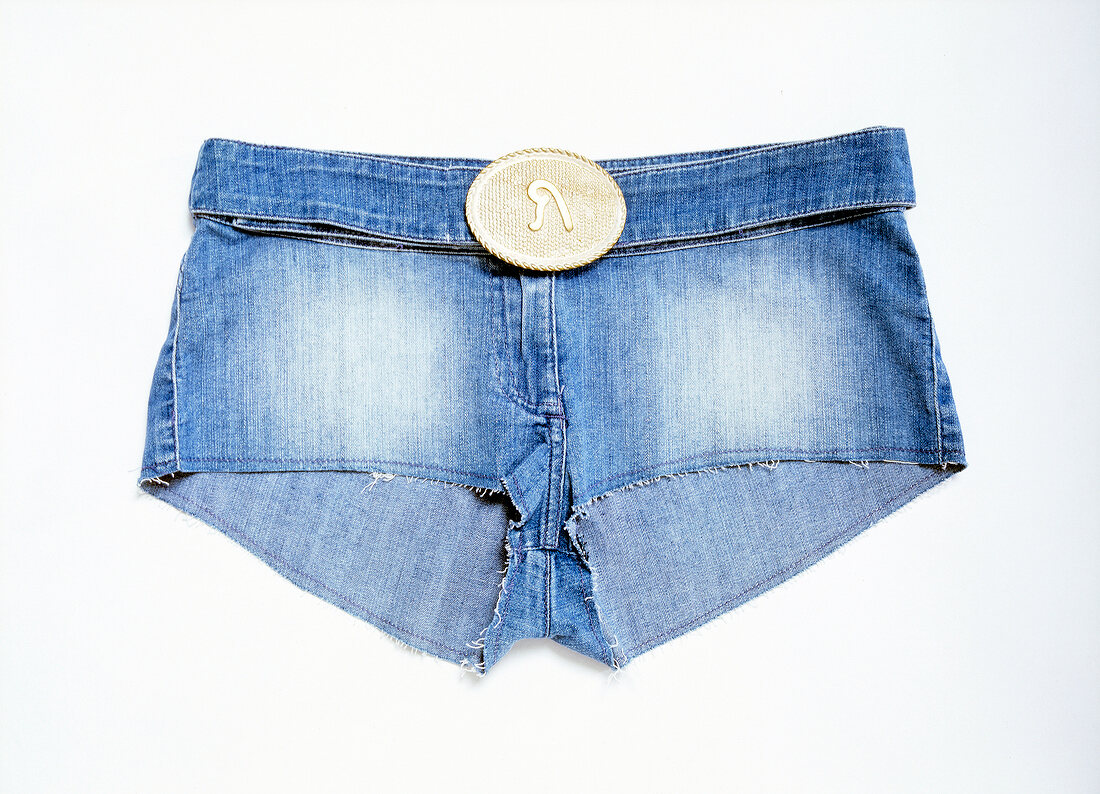 Close-up of pair of blue denim hot pants with oval buckle on white background