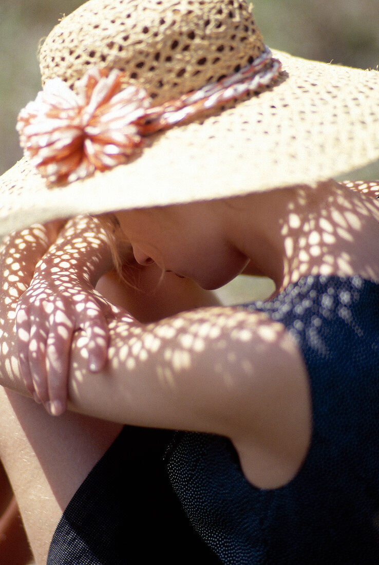 Sad woman wearing straw hat sitting with head down