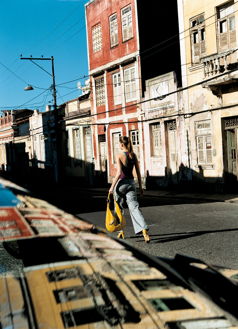 Frau mit Pferdeschwanz, Tasche gelb, auf der Straße, Rückenansicht.