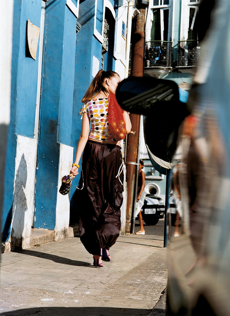 Woman wearing polka dots top walking on street while carrying mesh bag on shoulder