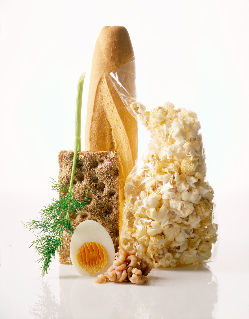 Bag of popcorn with half egg , crisp bread, French bread and spring of dill on white floor