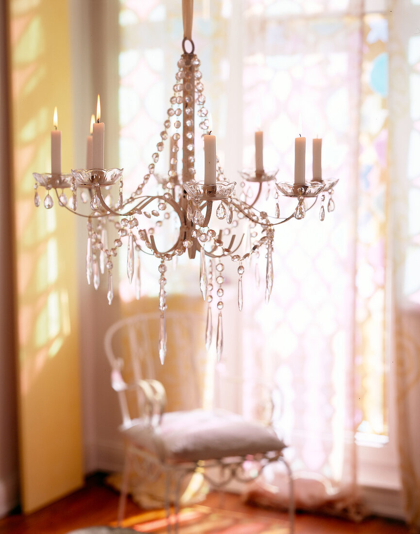 Lit candles on chandelier decorated with glass ornaments in living room