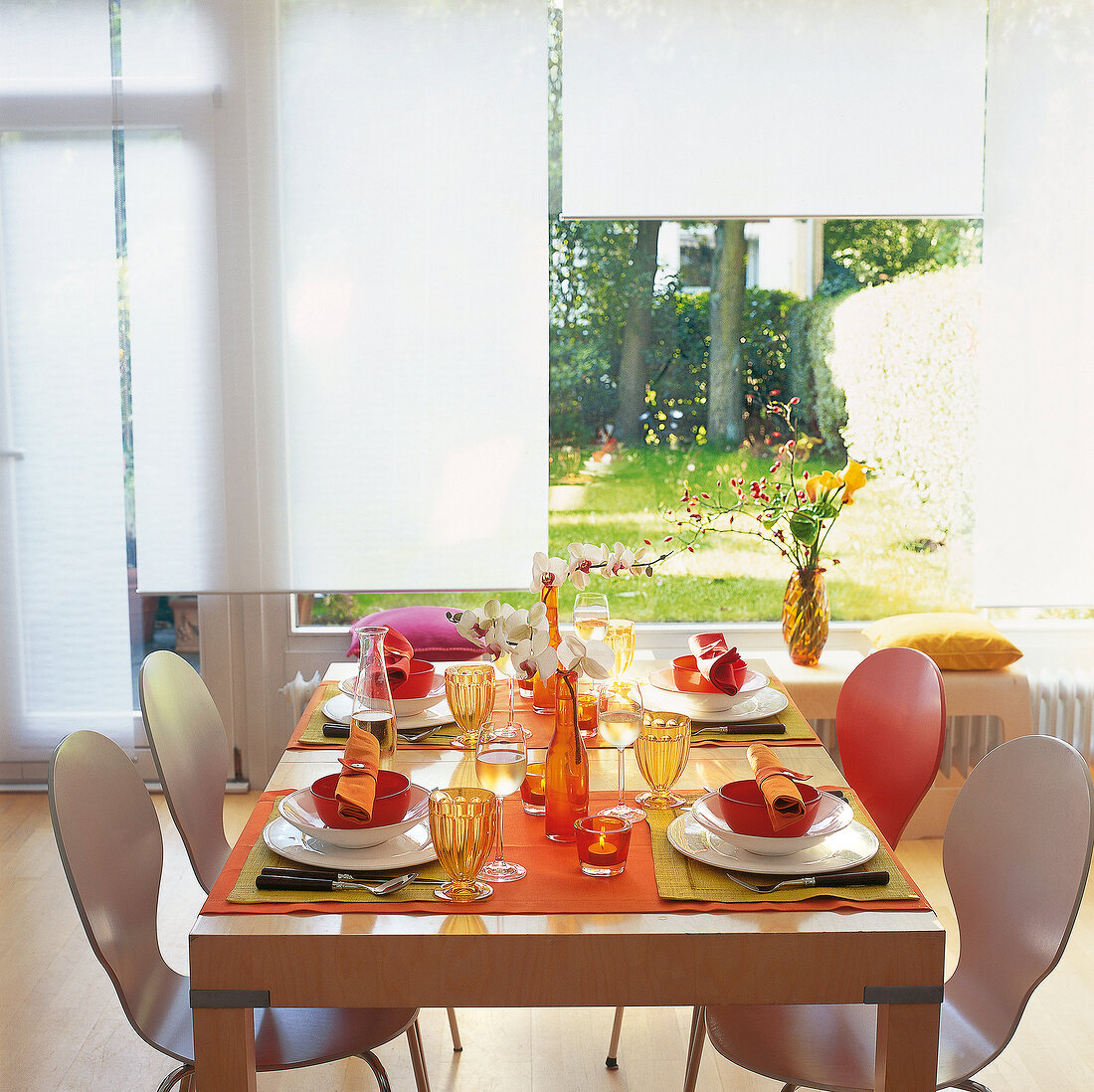 Table for four laid with orange crockery, vase with orchids on window sill