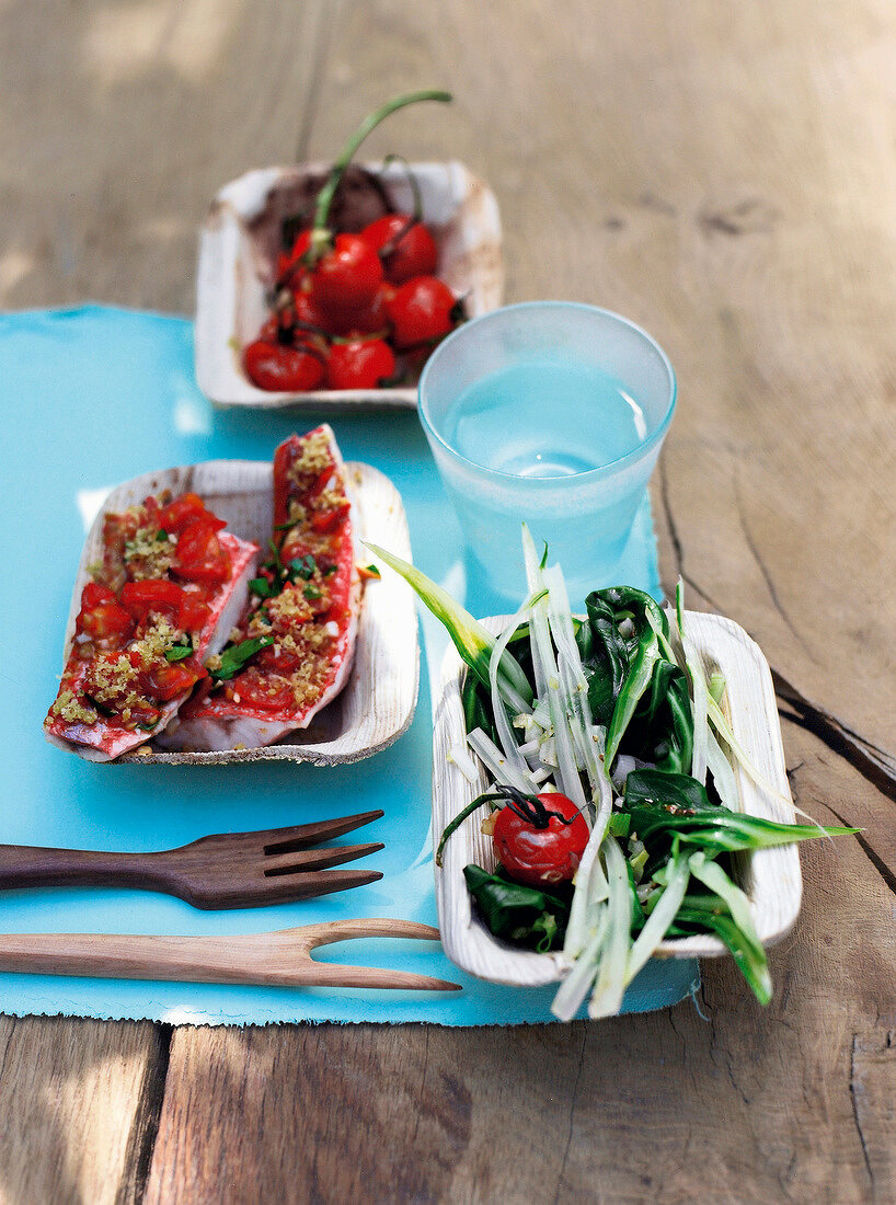 Baked fish fillet with tomatoes and salad on paper plate