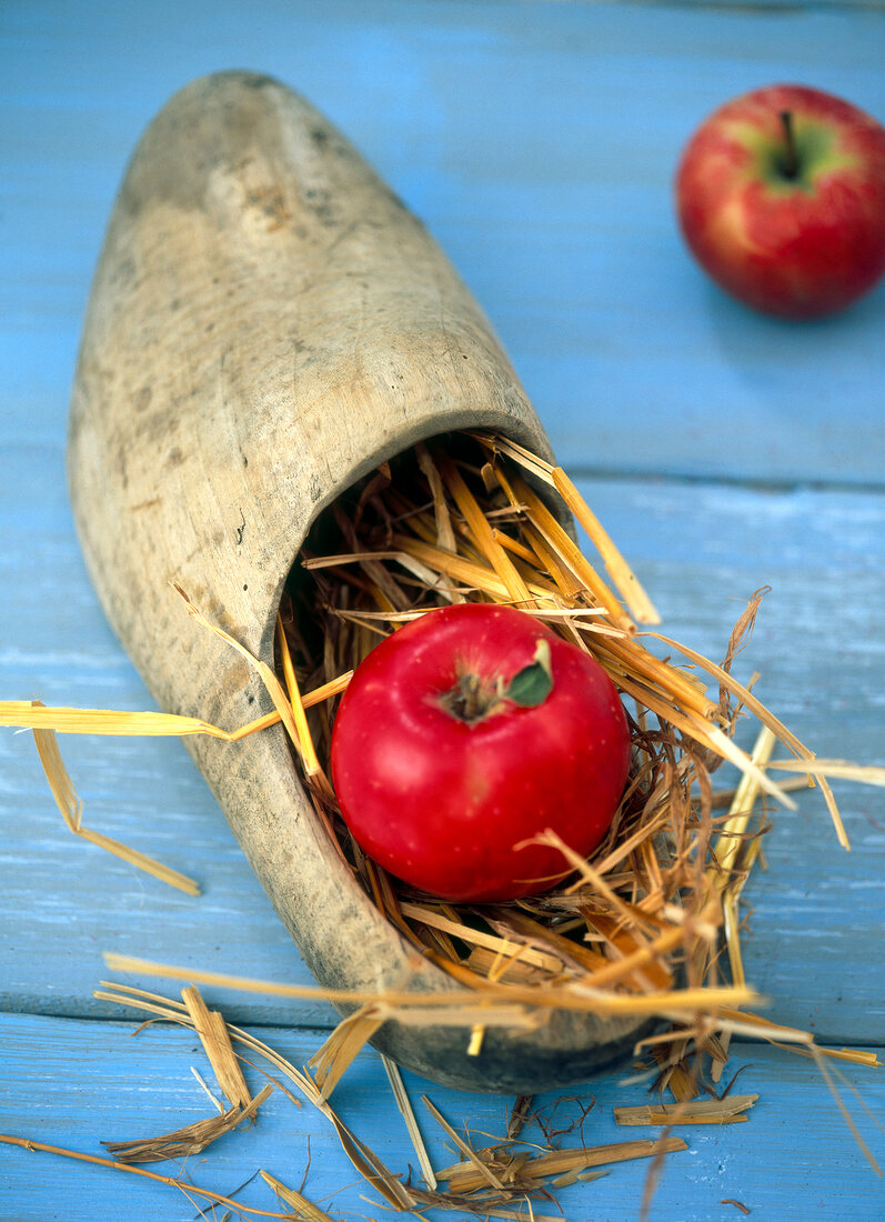 Close-up of red apple and straw in wooden shoe on blue background