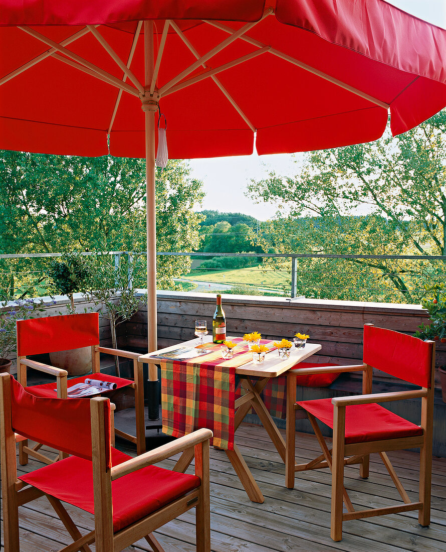 Dining table with chairs under red parasol on roof terrace