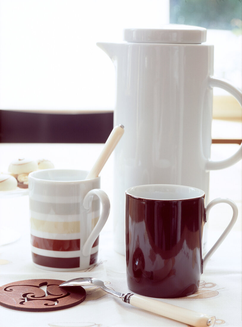 weiße Kaffeekanne mit einer braunen und einer gestreiften Tasse.x