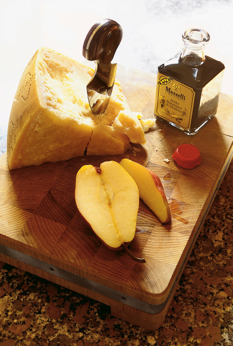Parmesan, Birnenstücke und eine Flasche Essig auf einem Holzbrett.