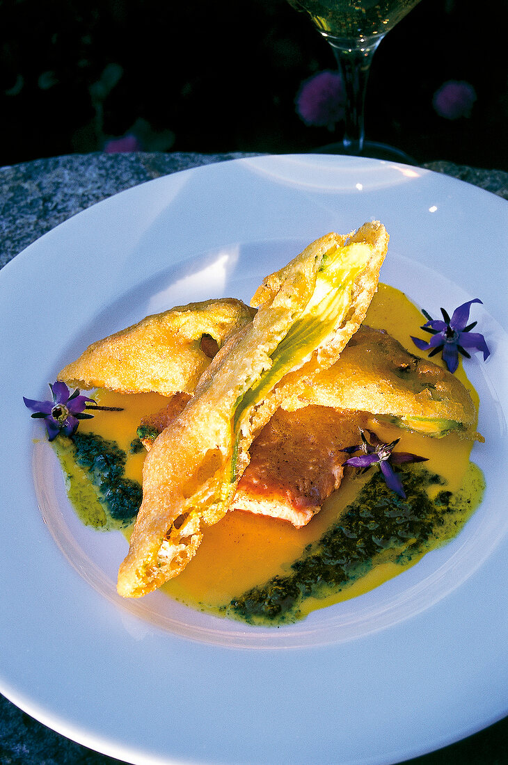 Close-up of salmon trout with fried zucchini and flowers on plate