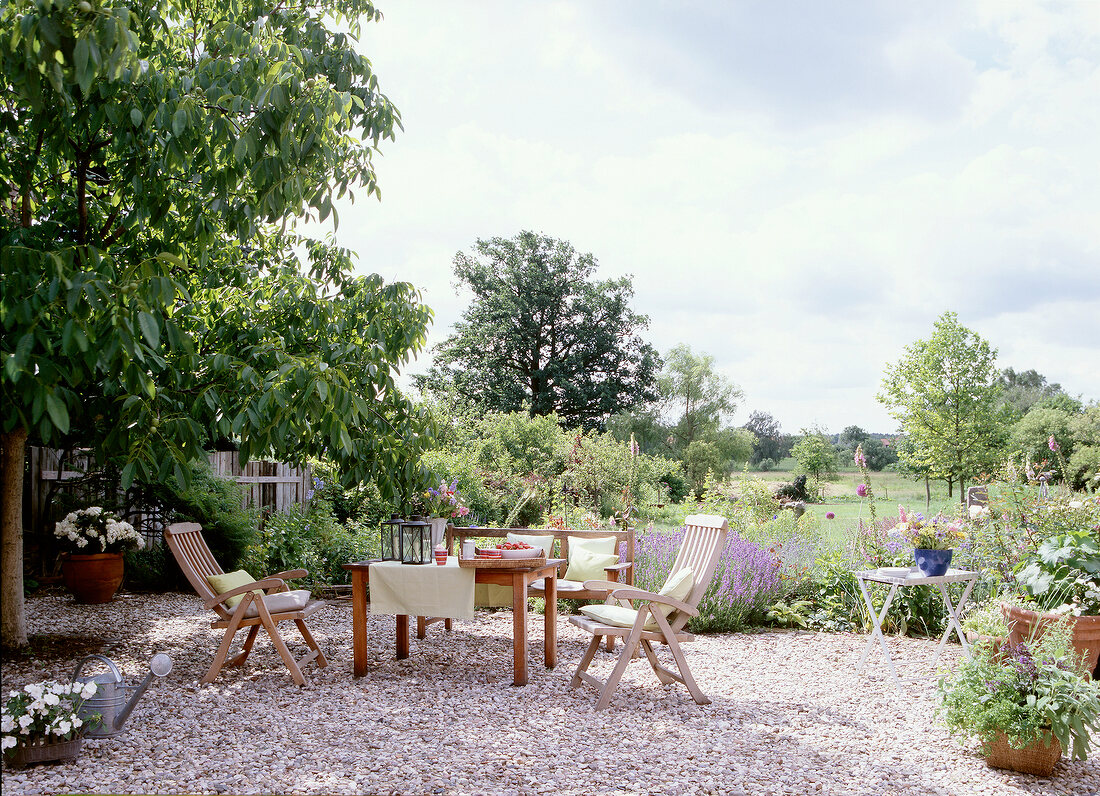 Table with wooden chairs and cushions on gravel surface in garden of an old manor