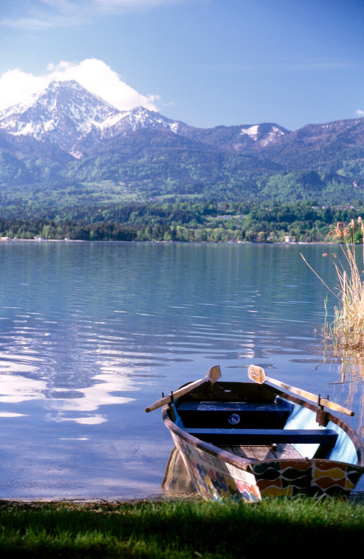 View of mountains overlooking boat moored near shore of Lake Worth, Austria