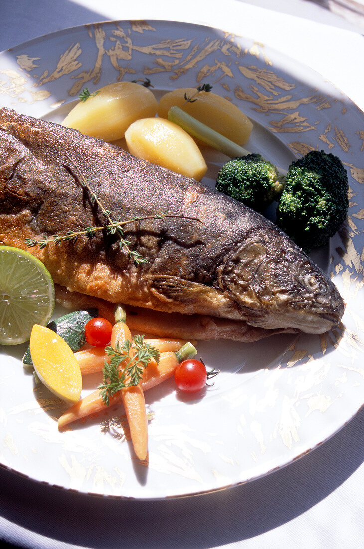Close-up of fish with potatoes, carrots and broccoli on plate
