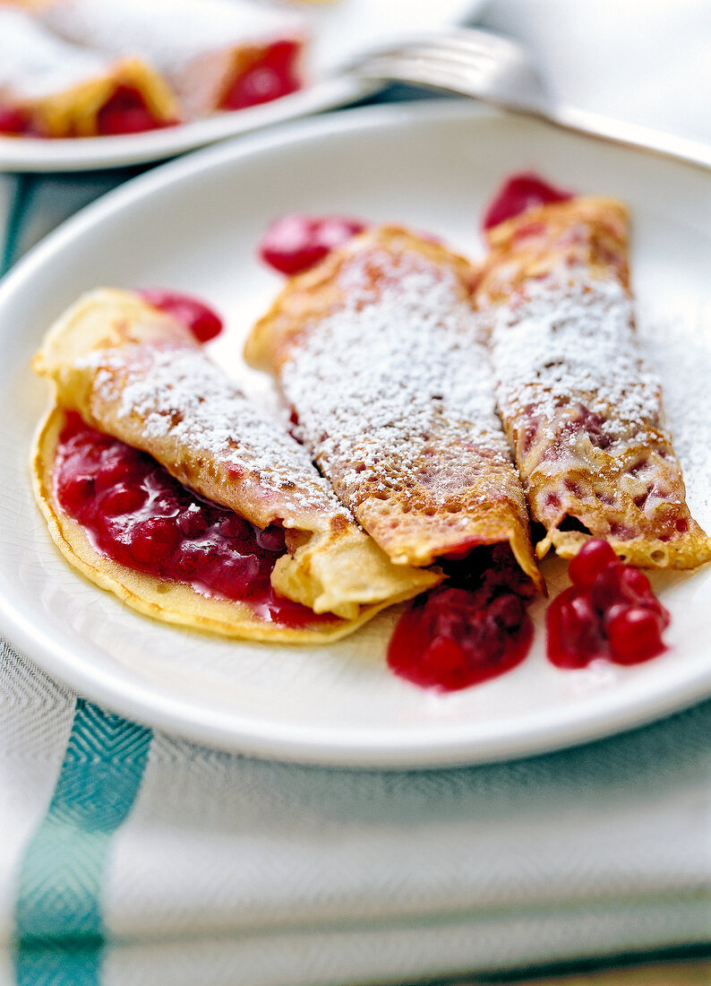 Three lingonberry crepes with sugar powder on plate